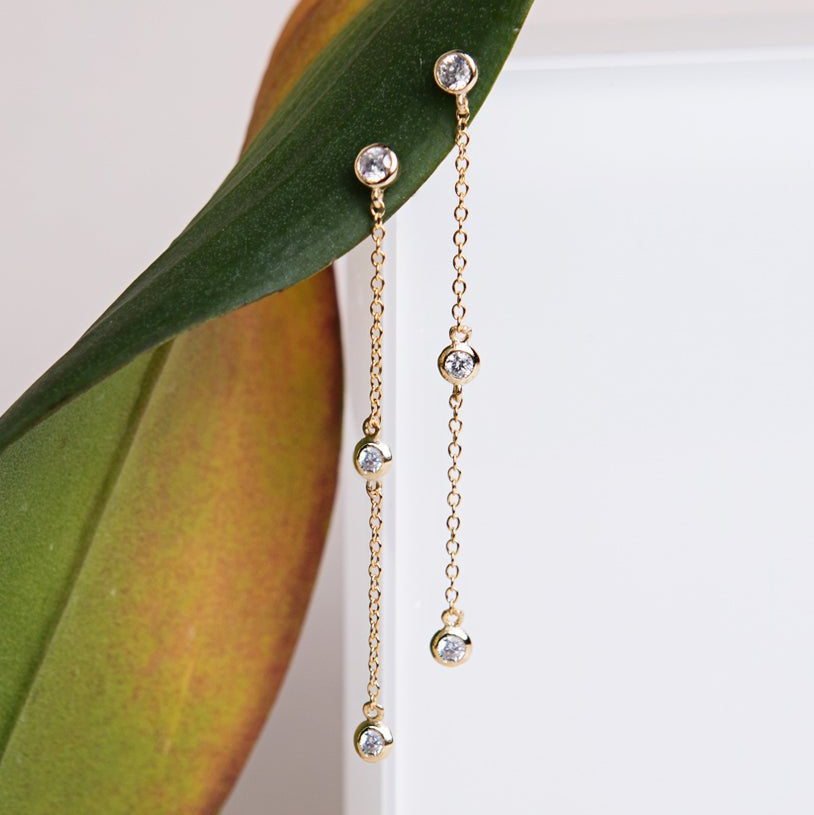 Gold vermeil white zirconia drop earrings staggered along chain, resting against a green leaf