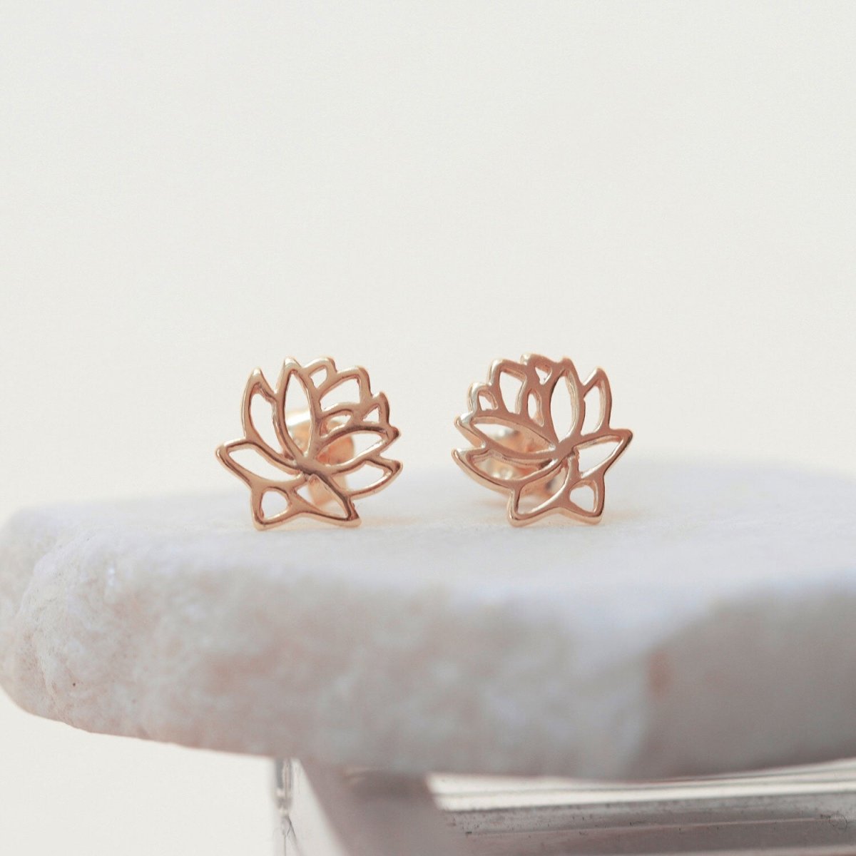 Rose gold vermeil lotus flower stud earrings, close-up detail on a stone surface