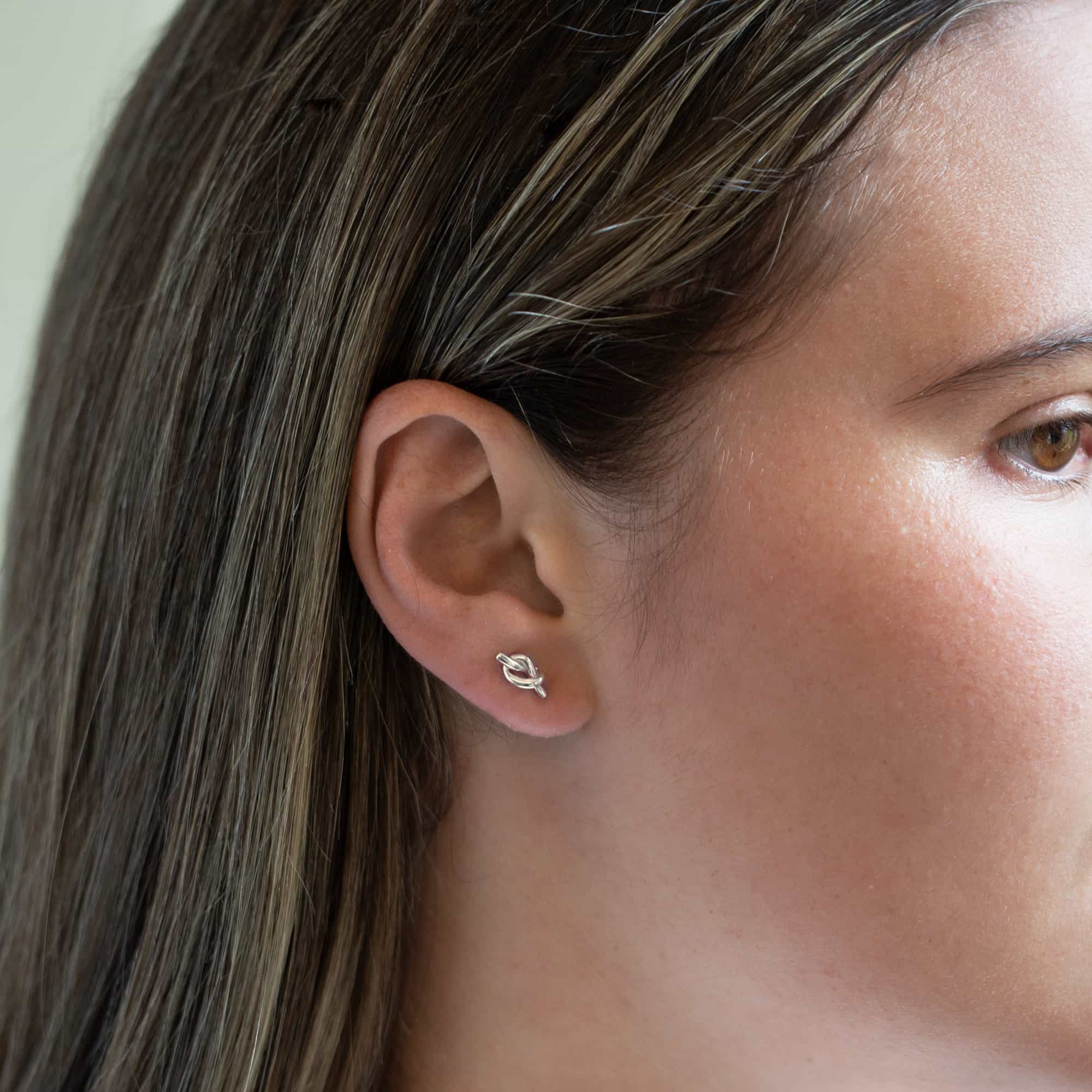 Sterling silver knot stud earring with a tiny love-knot design, shown on a model's lobe