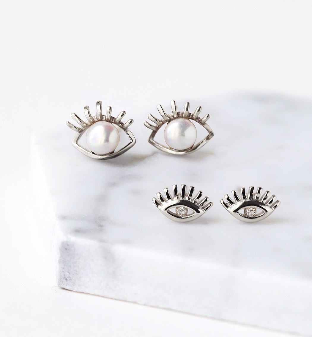 Sterling silver evil eye studs with pearl and clear-stone versions, shown on white marble