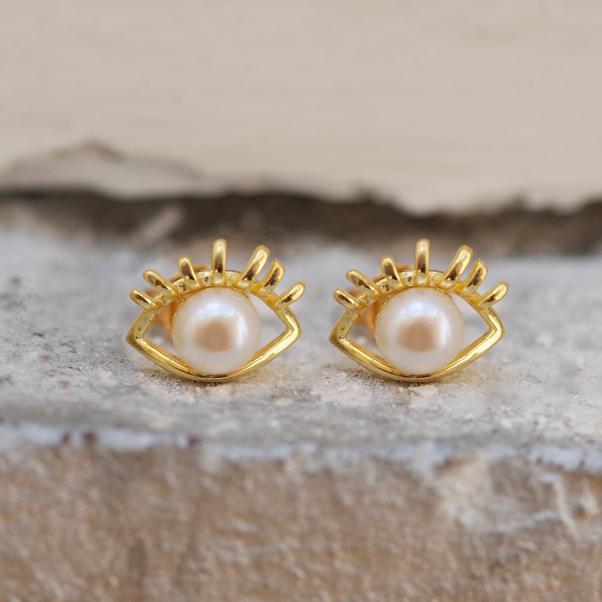Gold vermeil evil eye stud earrings with white pearl centers, shown on white stone