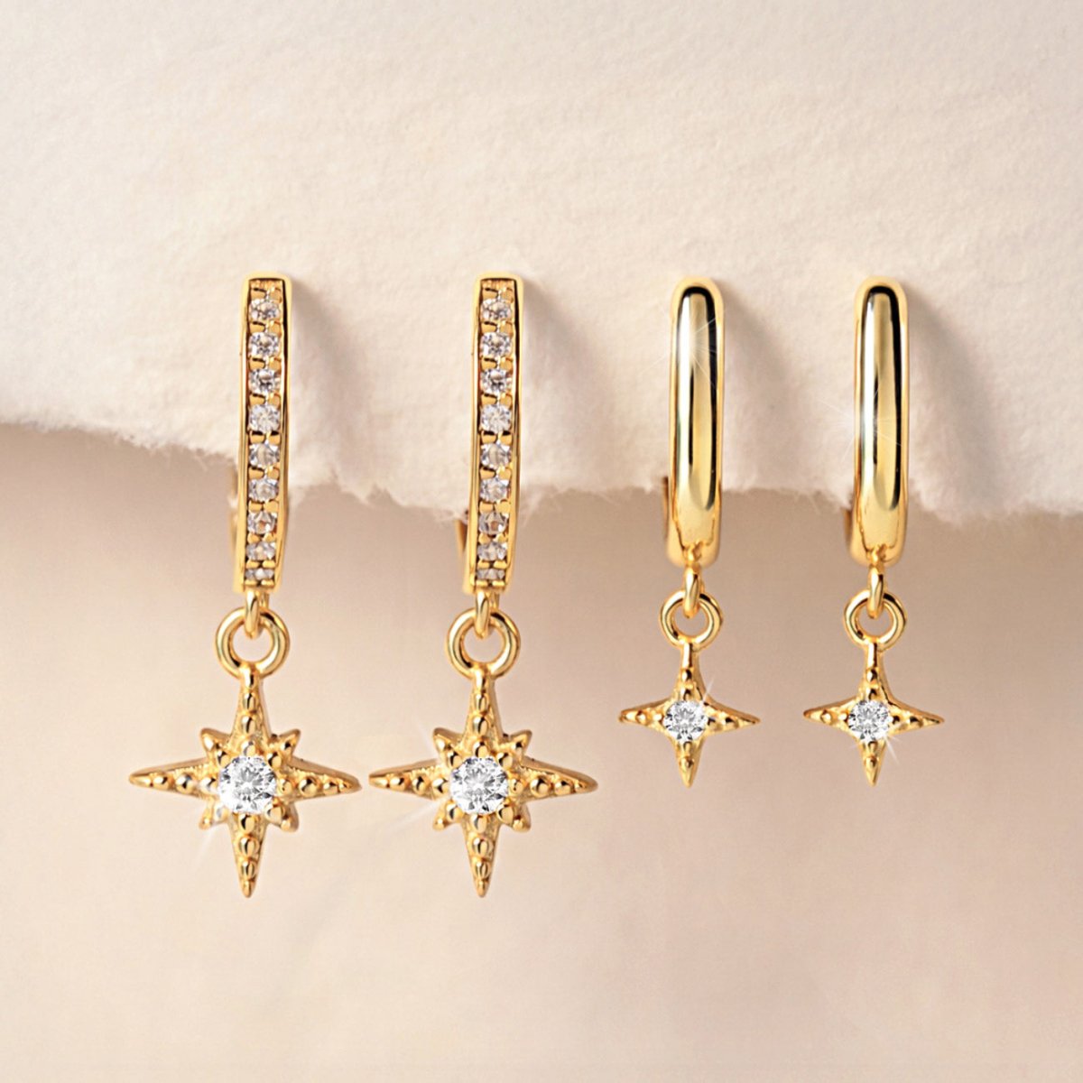 Gold vermeil starburst pavé drop huggie hoops with clear stones, shown on a cream background