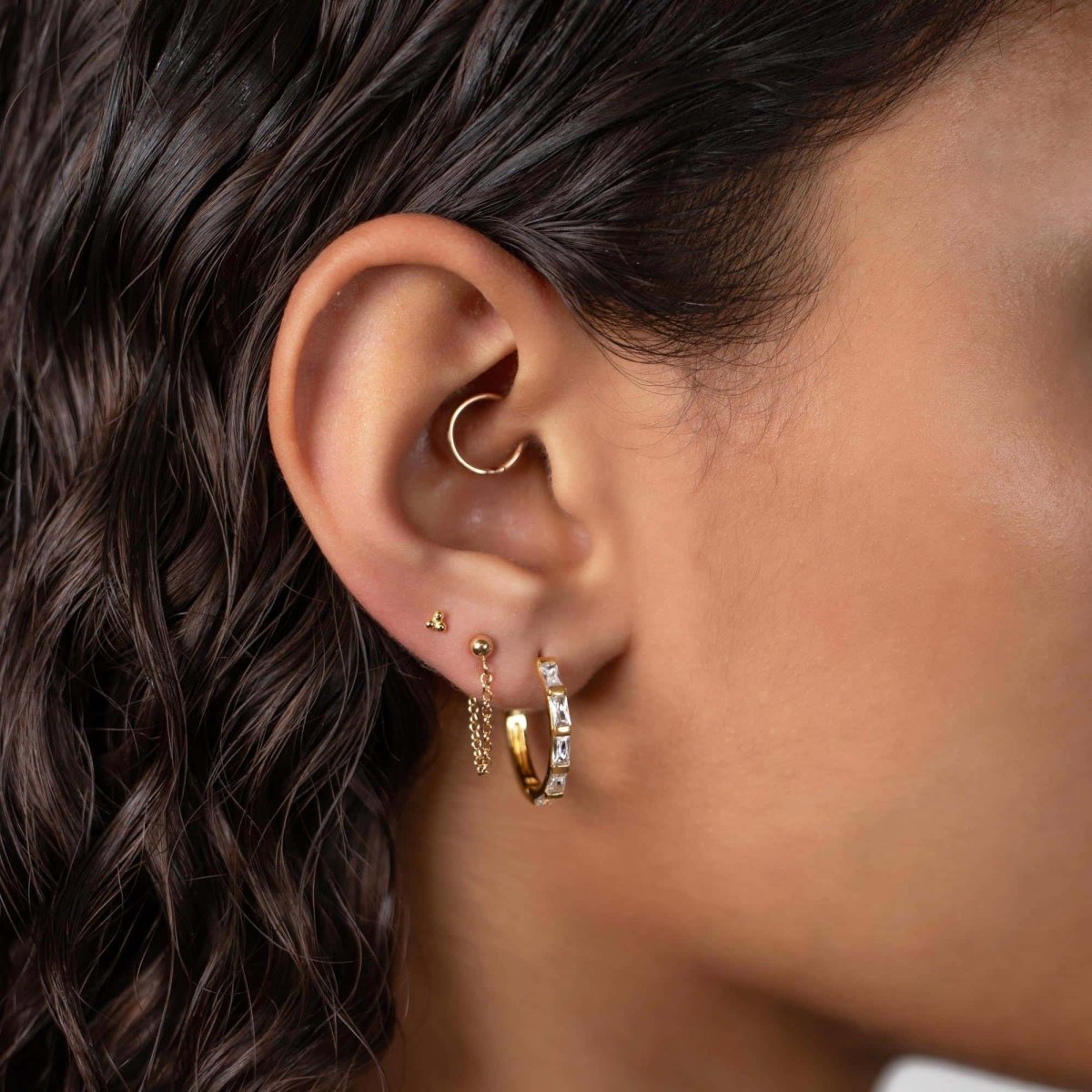 Gold titanium trinity-bead flat back stud shown in a lobe stack with hoops on a model