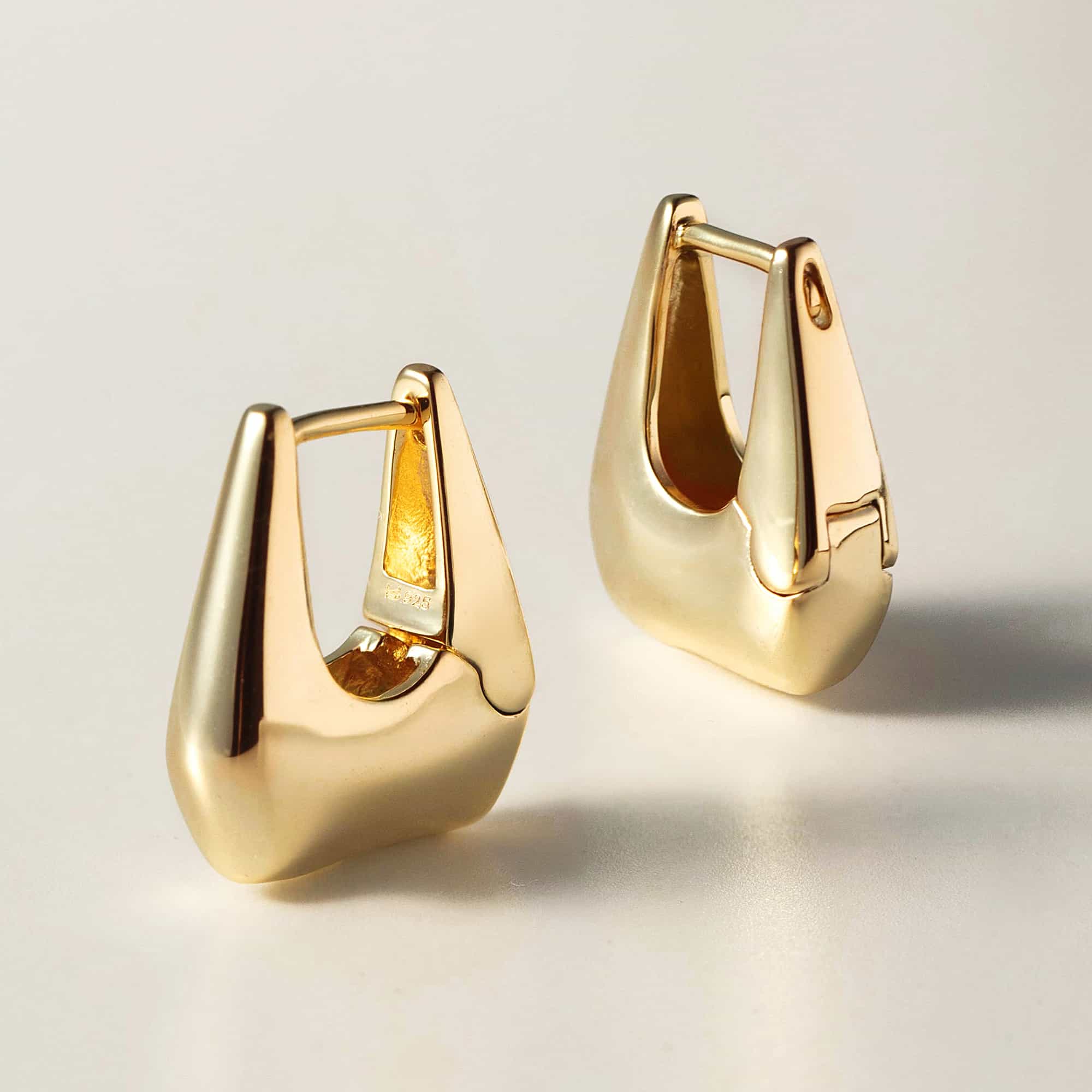Gold vermeil chunky tapered huggie hoops, close-up detail on a pale gray surface