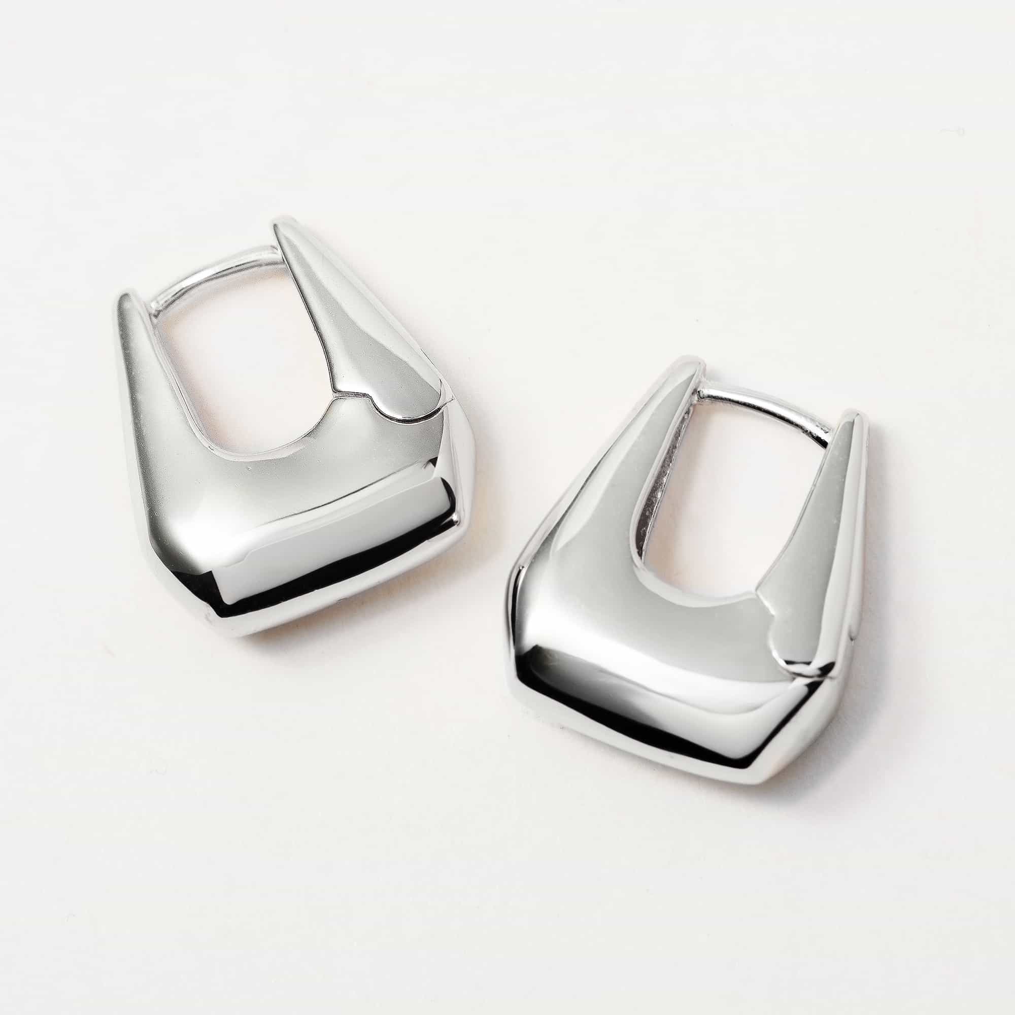 Sterling silver chunky tapered huggie hoops, close-up detail on a pale gray surface