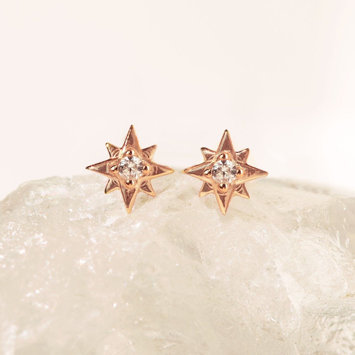 Pair of rose gold vermeil star studs with white zirconia stones, on a white crystal surface