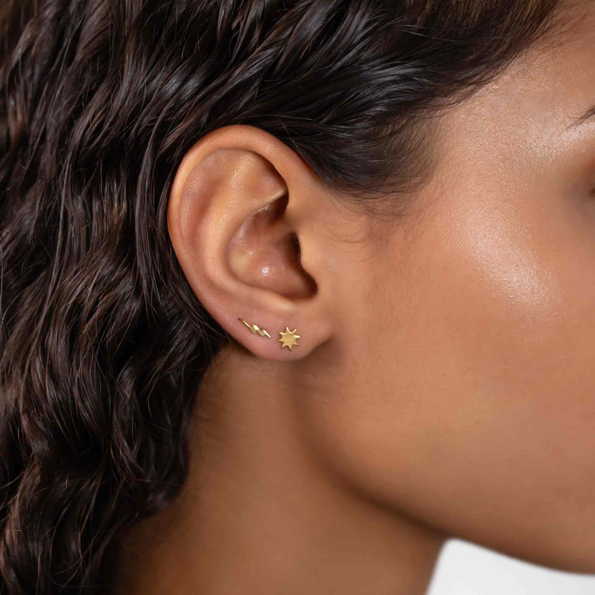 Gold vermeil sunburst star stud shown in a model's lobe with a small lightning-bolt stud