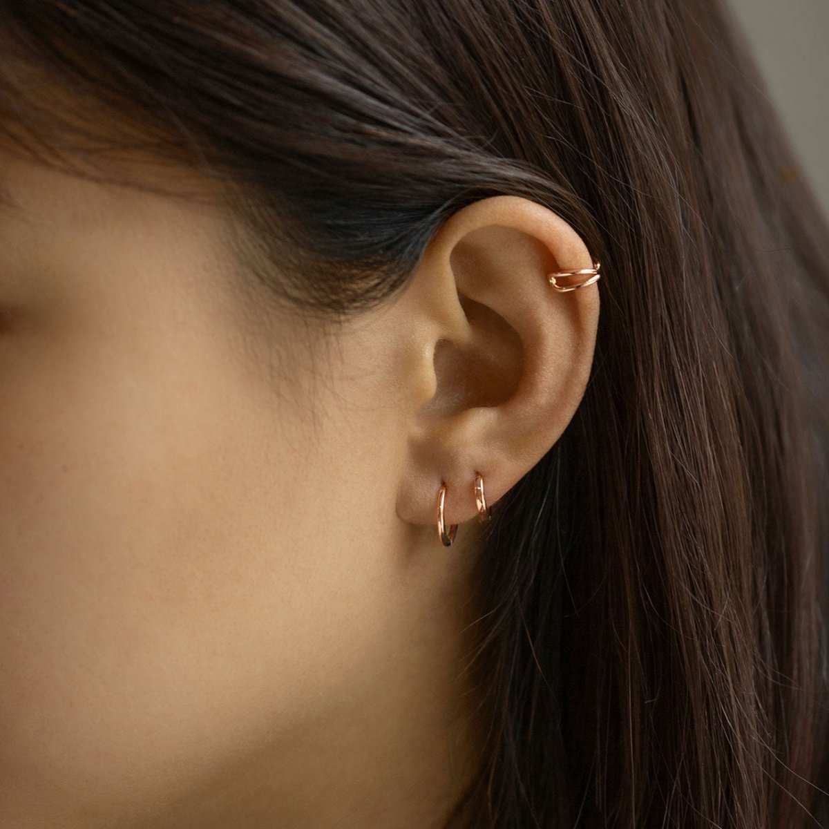 Rose gold vermeil criss-cross ear cuff shown on a model's upper ear above hoops