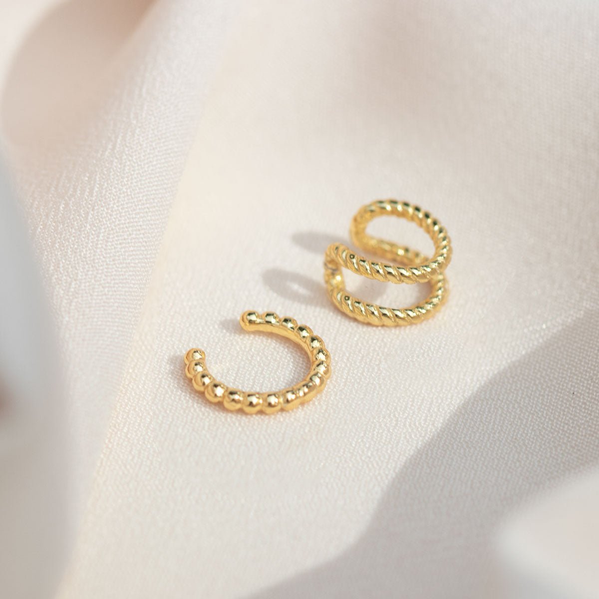Gold vermeil beaded ear cuff beside a twisted-rope cuff, laid on cream fabric