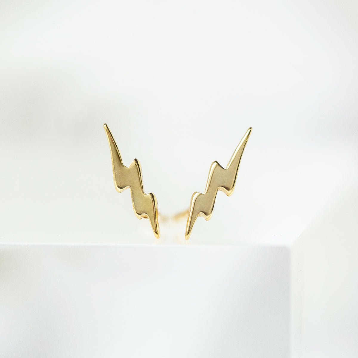 Gold vermeil tiny lightning bolt studs shown upright as a pair against a soft white prop