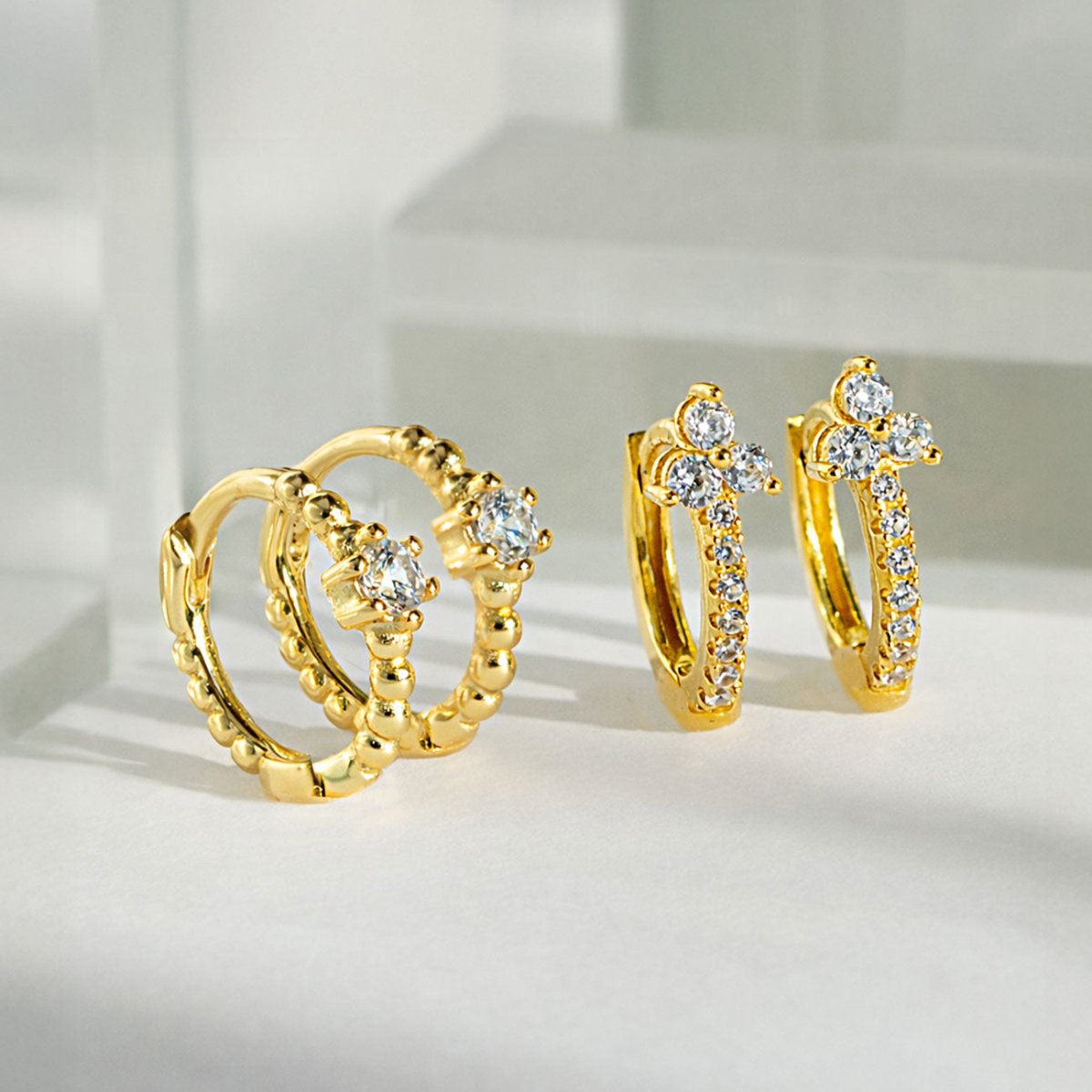 Gold vermeil pavé huggie hoops with clear zirconia, shown beside beaded huggies on a white surface