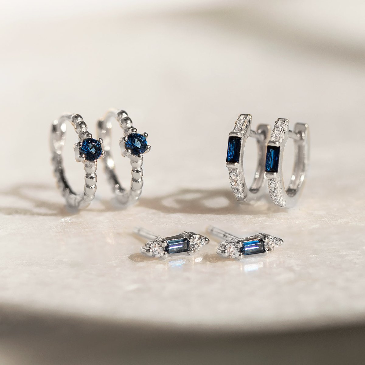 Sterling silver pieces with blue stones, including baguette studs, hoops and a ring, on white marble