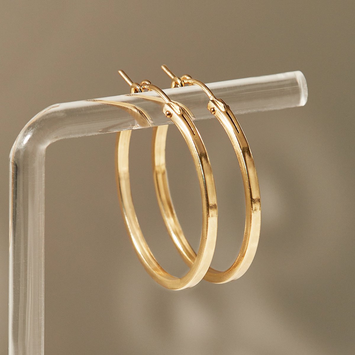 Gold-filled thin square-edge hoop earrings hung on a clear acrylic stand, close-up detail