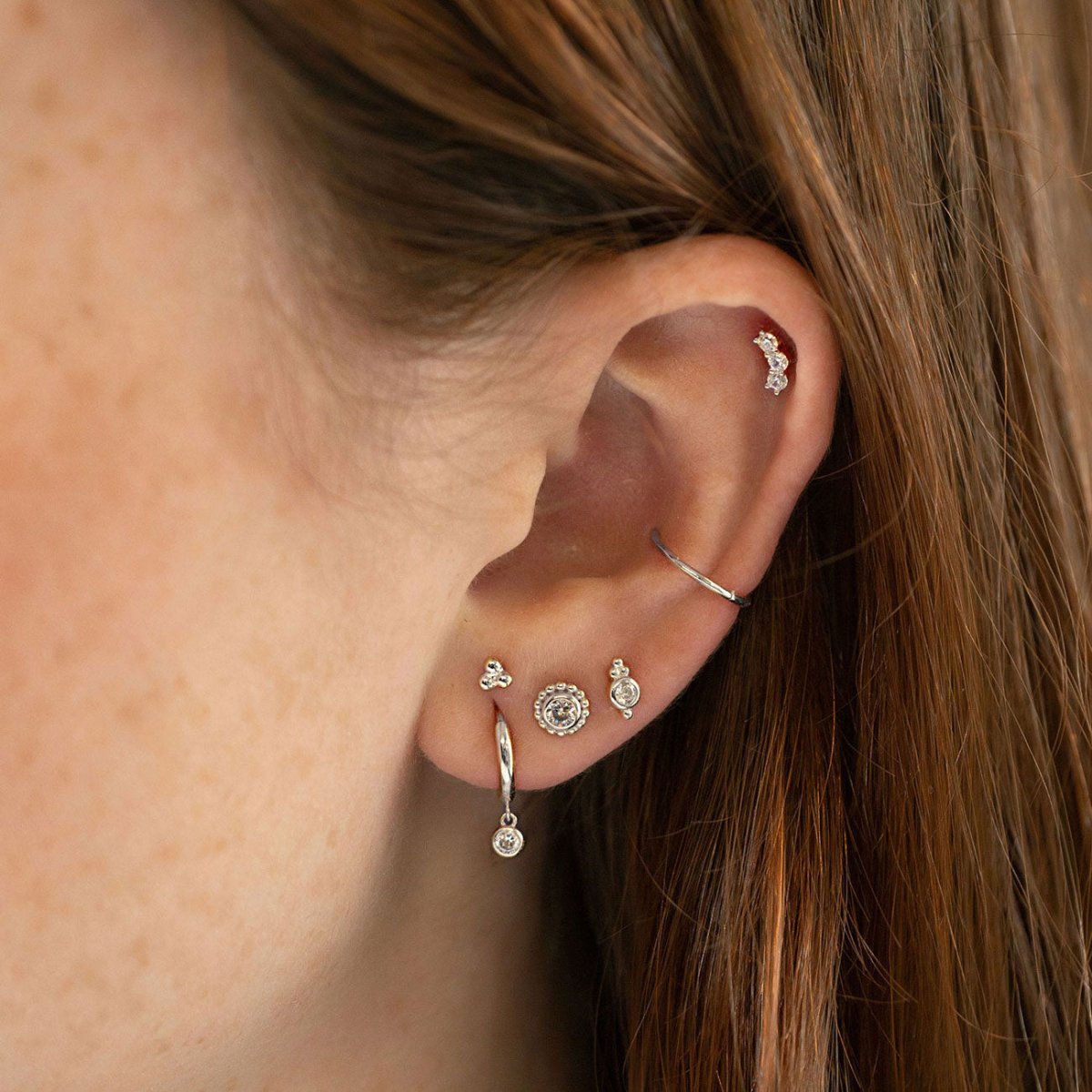 Silver studs, huggie hoops and a cuff with clear stones, styled in an ear stack on a model