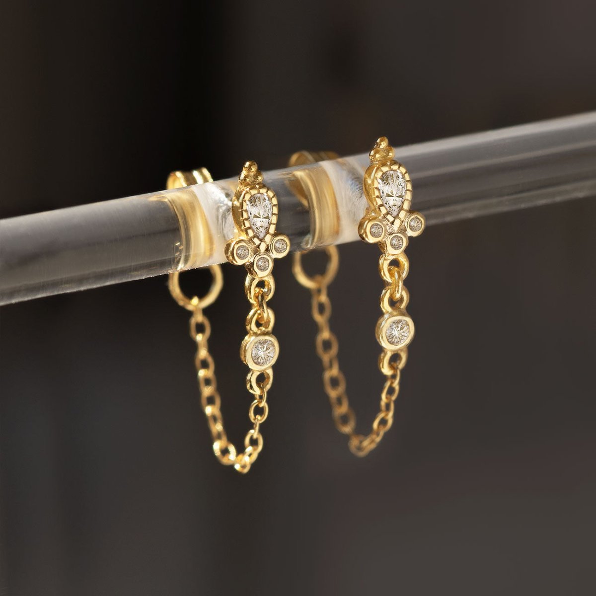 Gold vermeil chain-wrap stud earrings with white zirconia, close-up detail on a clear stand