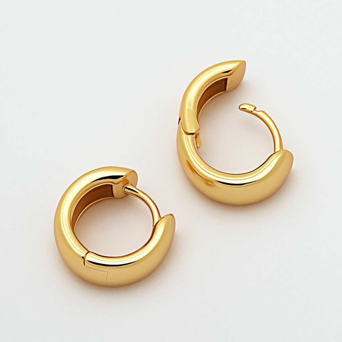 Gold vermeil chunky rounded mini huggie hoop earrings with a hinged closure, on a white background