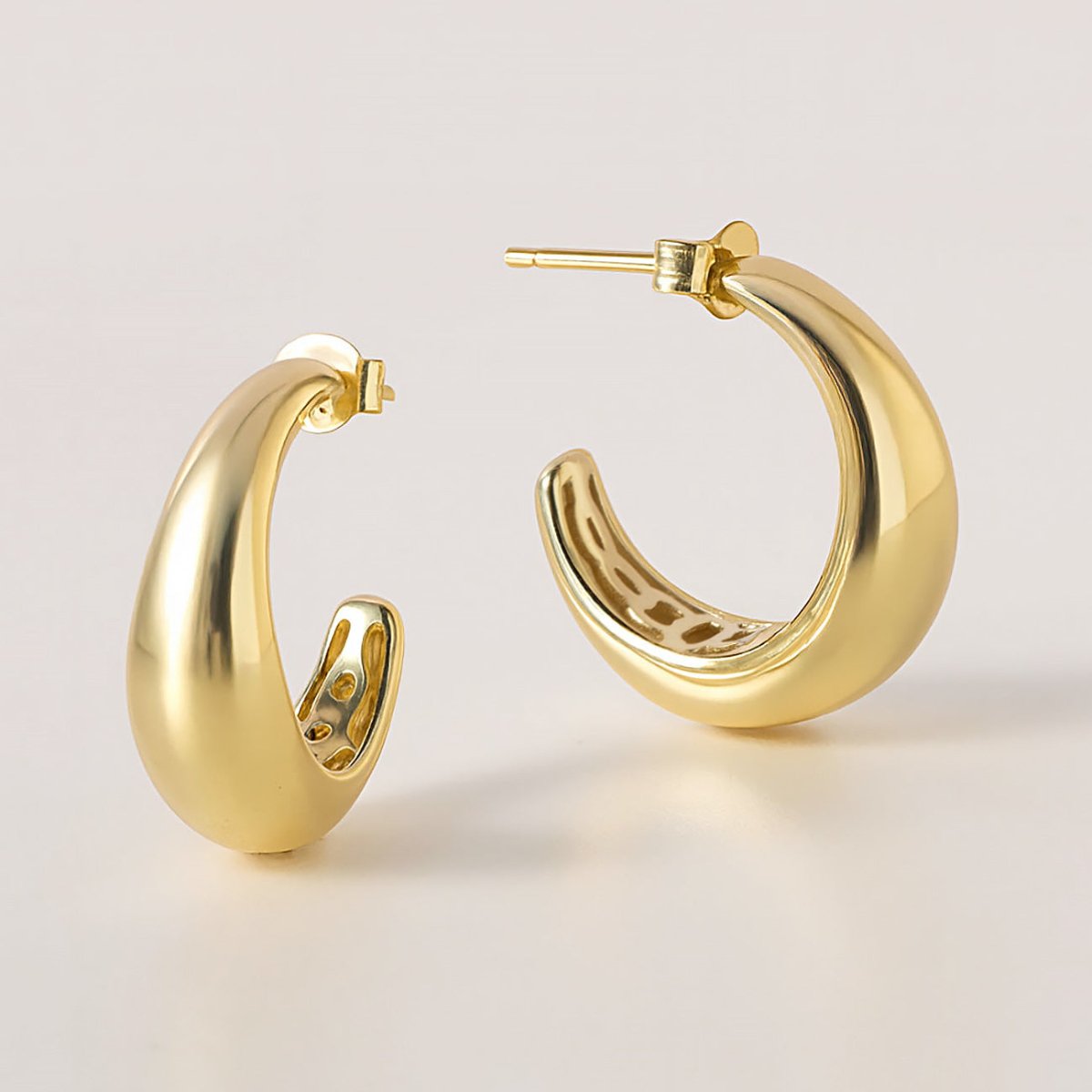 Gold vermeil tapered C-shaped hoop earrings, three-quarter view on a cream surface