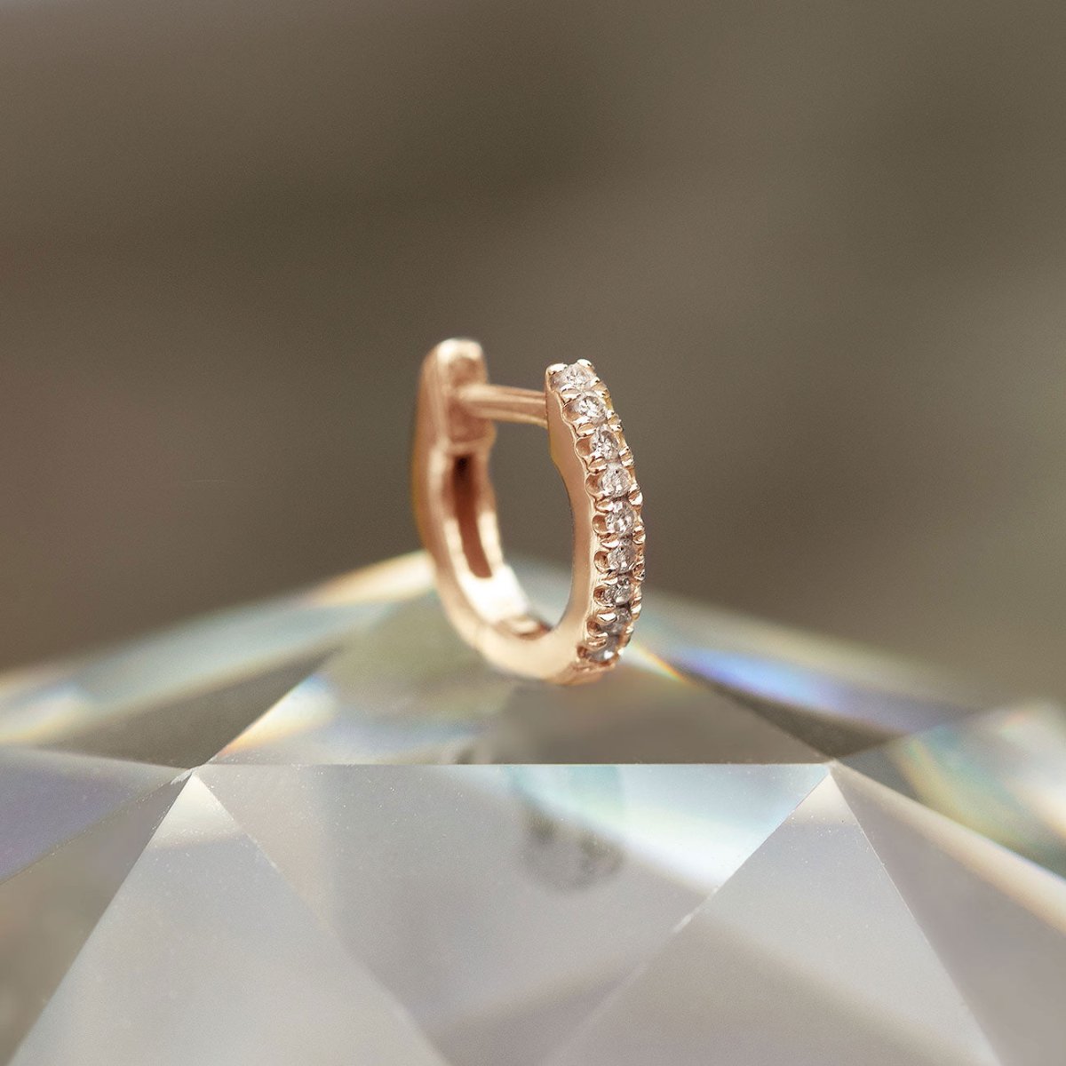 14K rose gold pavé diamond huggie hoop resting on a faceted crystal, close-up detail