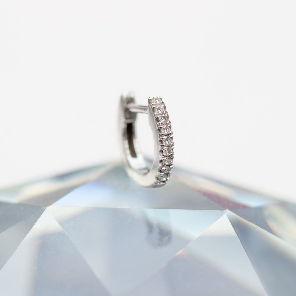 14K white gold pavé diamond huggie hoop resting on a faceted crystal, close-up detail