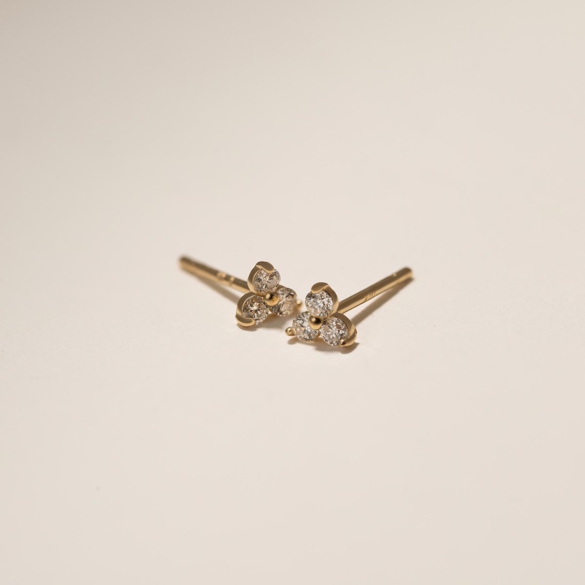 Pair of 14K gold diamond clover three-stone cluster studs with their posts, on a cream background