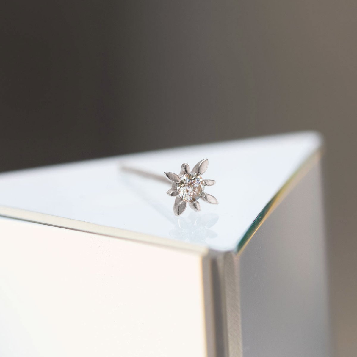 14K white gold starburst stud with a clear zirconia, close-up on a mirrored surface