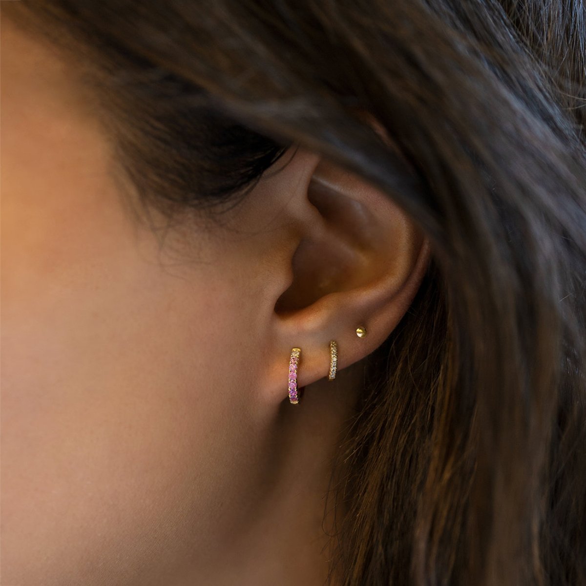 14K gold huggie hoop with ombre pink sapphire stones, shown on a model's lobe
