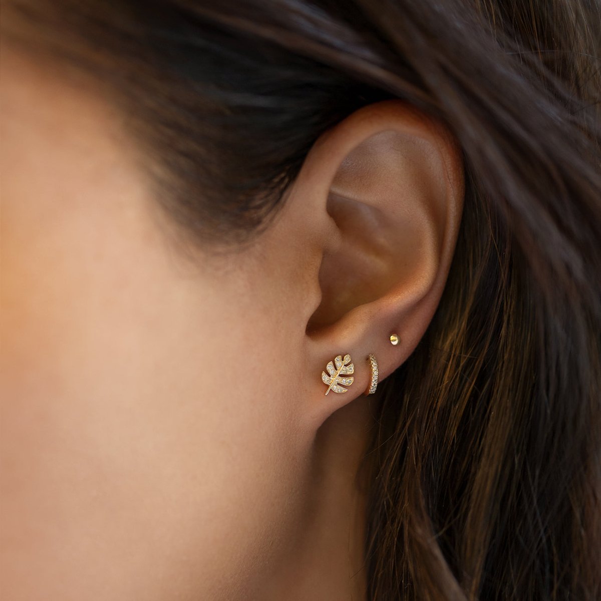 Gold diamond monstera leaf stud and thin hoop shown on a model's ear