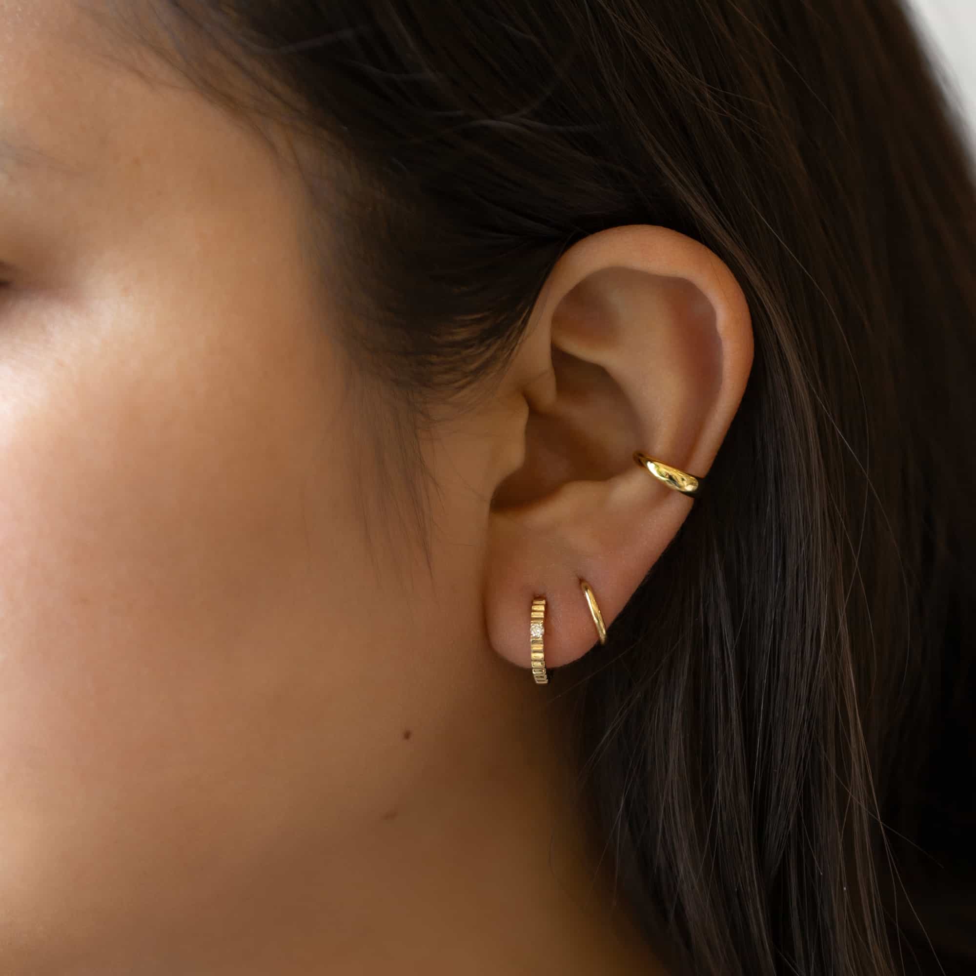 14K gold ridge-textured diamond huggie hoop with a plain hoop and ear cuff on a model's ear