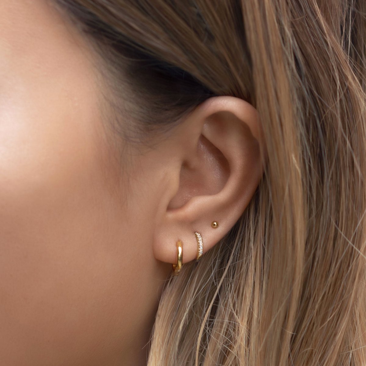 14K gold pavé diamond huggie shown on a model's lobe, stacked with plain gold hoops