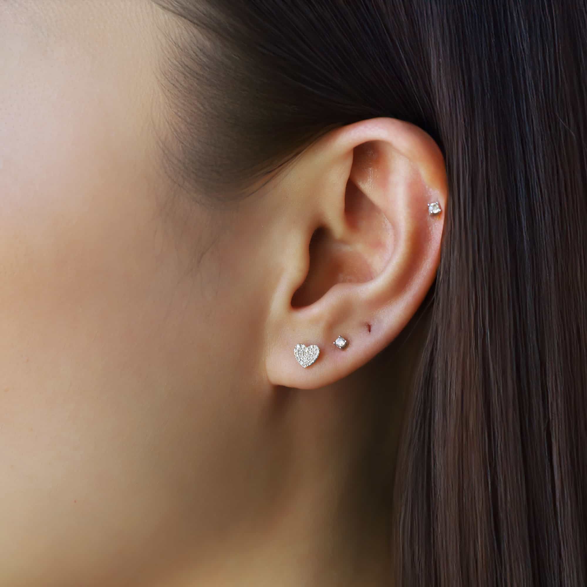 14K white gold pave diamond heart stud shown on a model's lobe beside a small round stud