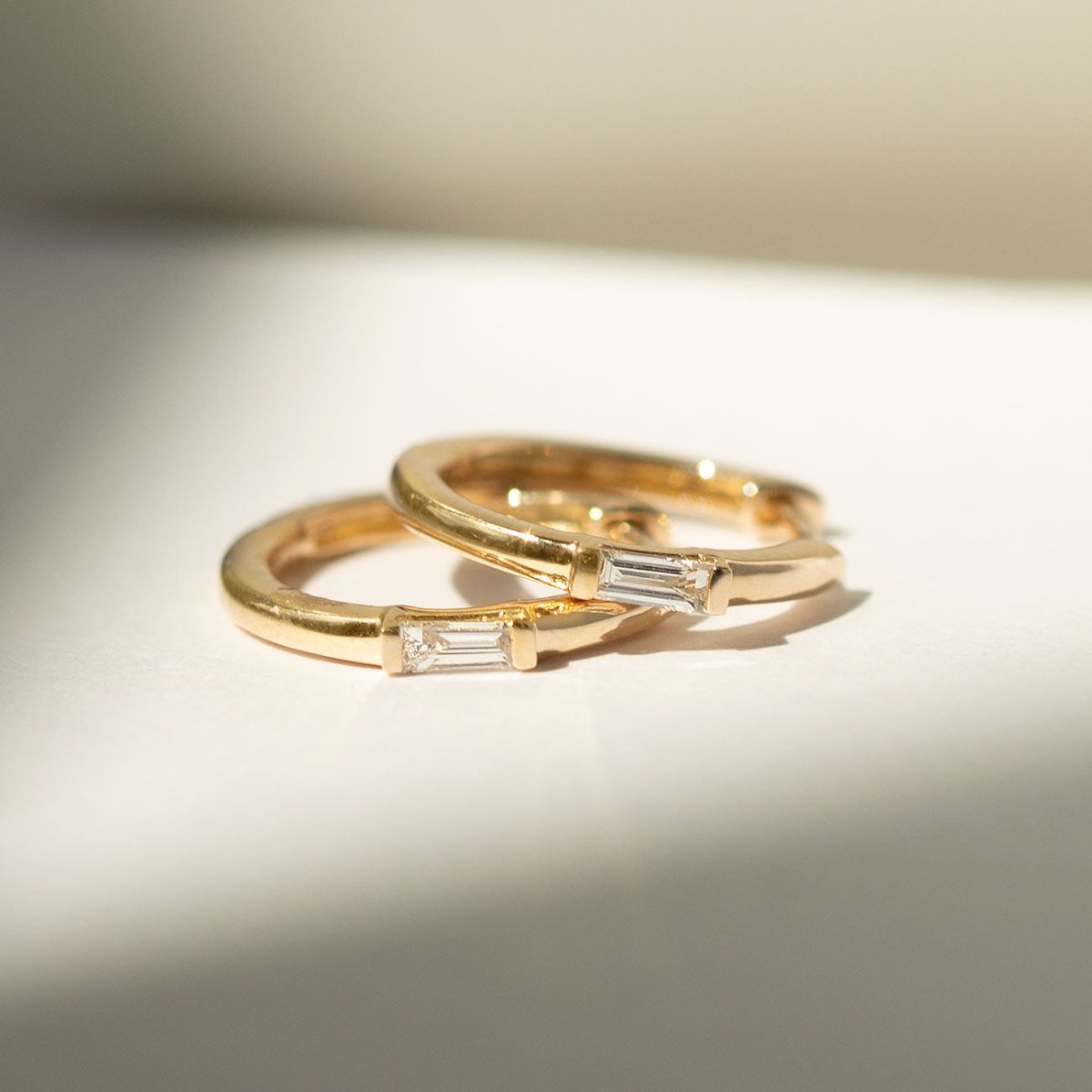14K gold huggie hoops with baguette diamonds, two hoops laid in warm light, close-up detail