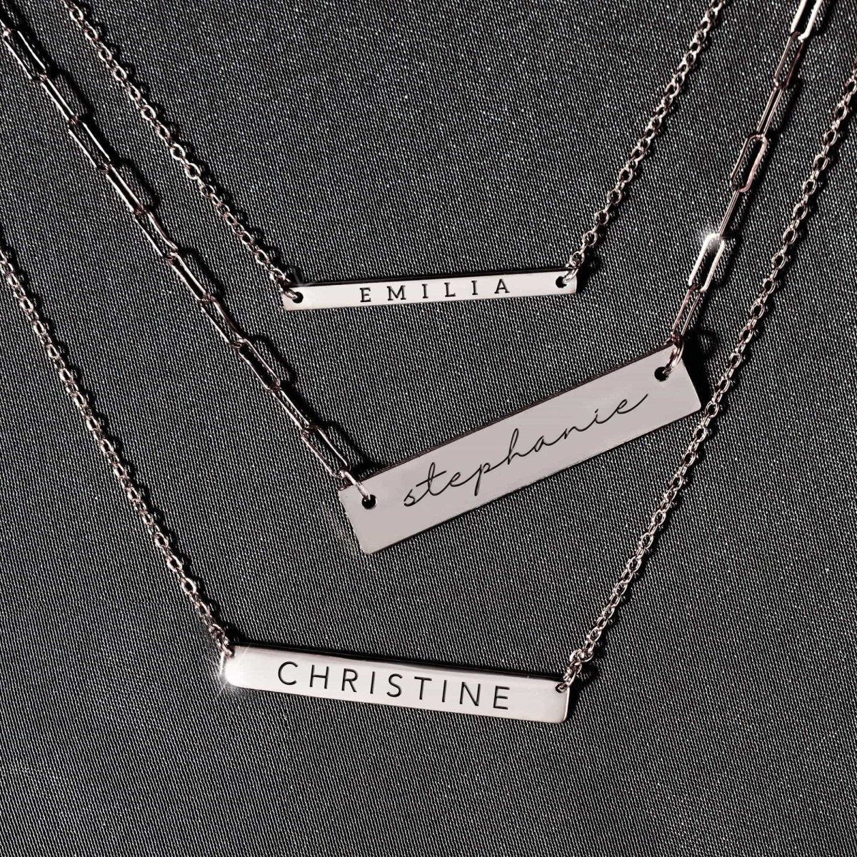 Sterling silver bar necklaces engraved with names, layered on a gray background