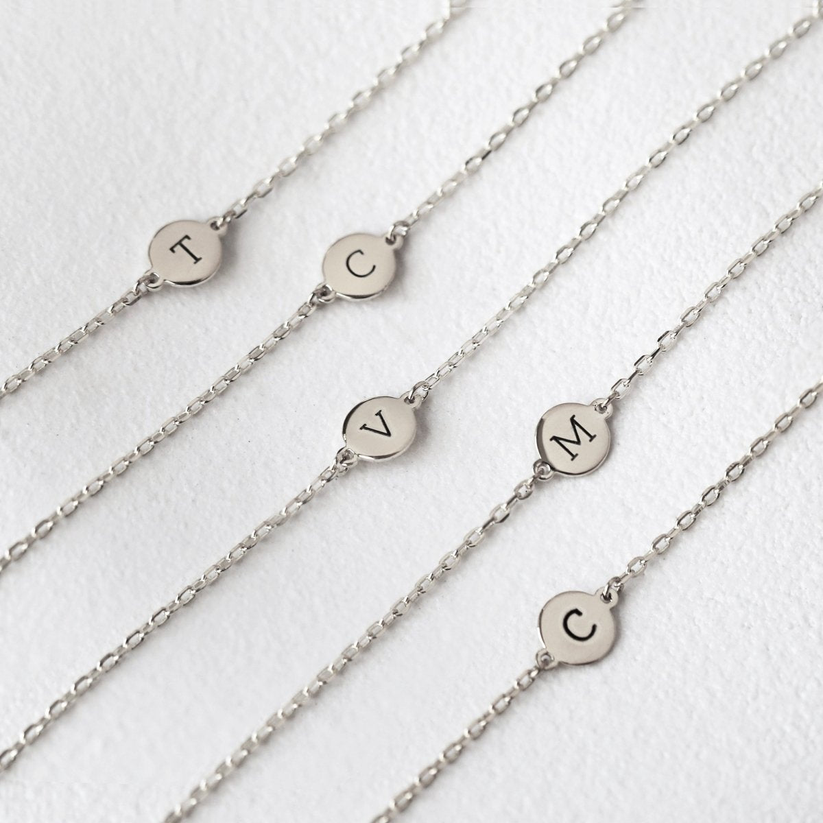 Sterling silver disc bracelets engraved with initials, laid in a row on a white background