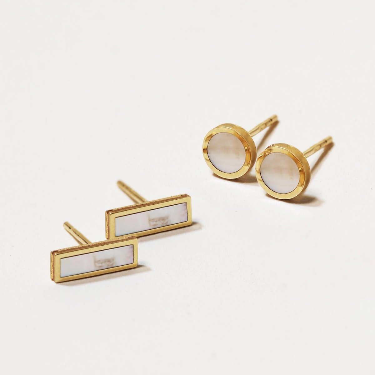 14K gold mother of pearl bar studs and round studs with pale iridescent inlay, on a white background