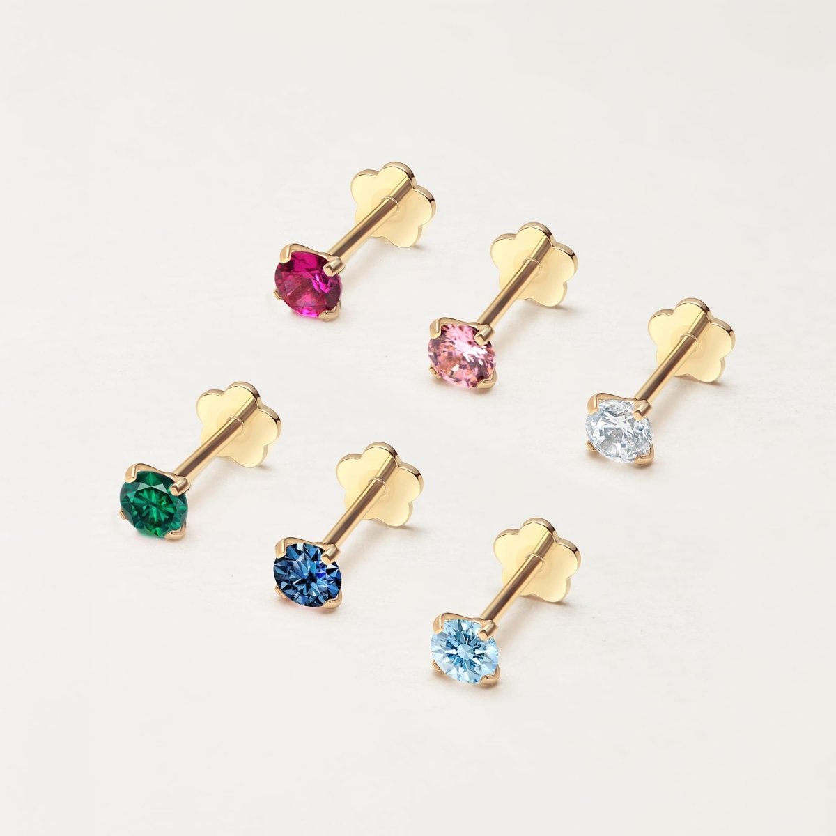 Six 14K gold flat back studs with round stones in mixed colors, including light blue aquamarine, on a cream background