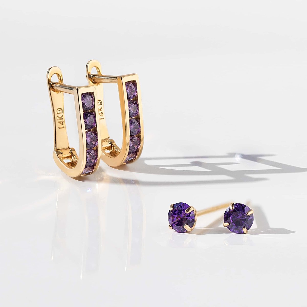 14K gold amethyst U huggie hoops beside matching purple stud earrings, on a white background