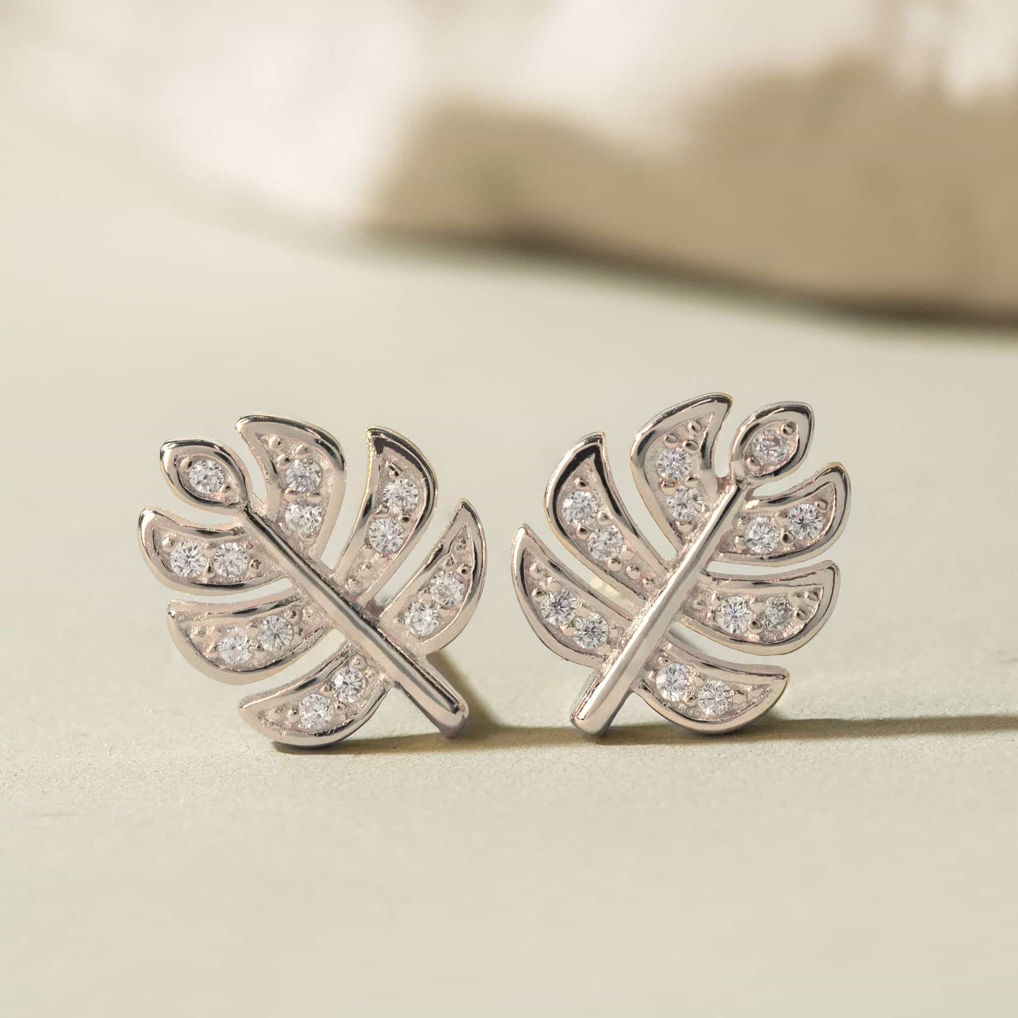 Sterling silver monstera leaf stud earrings with clear pave stones, on a cream surface