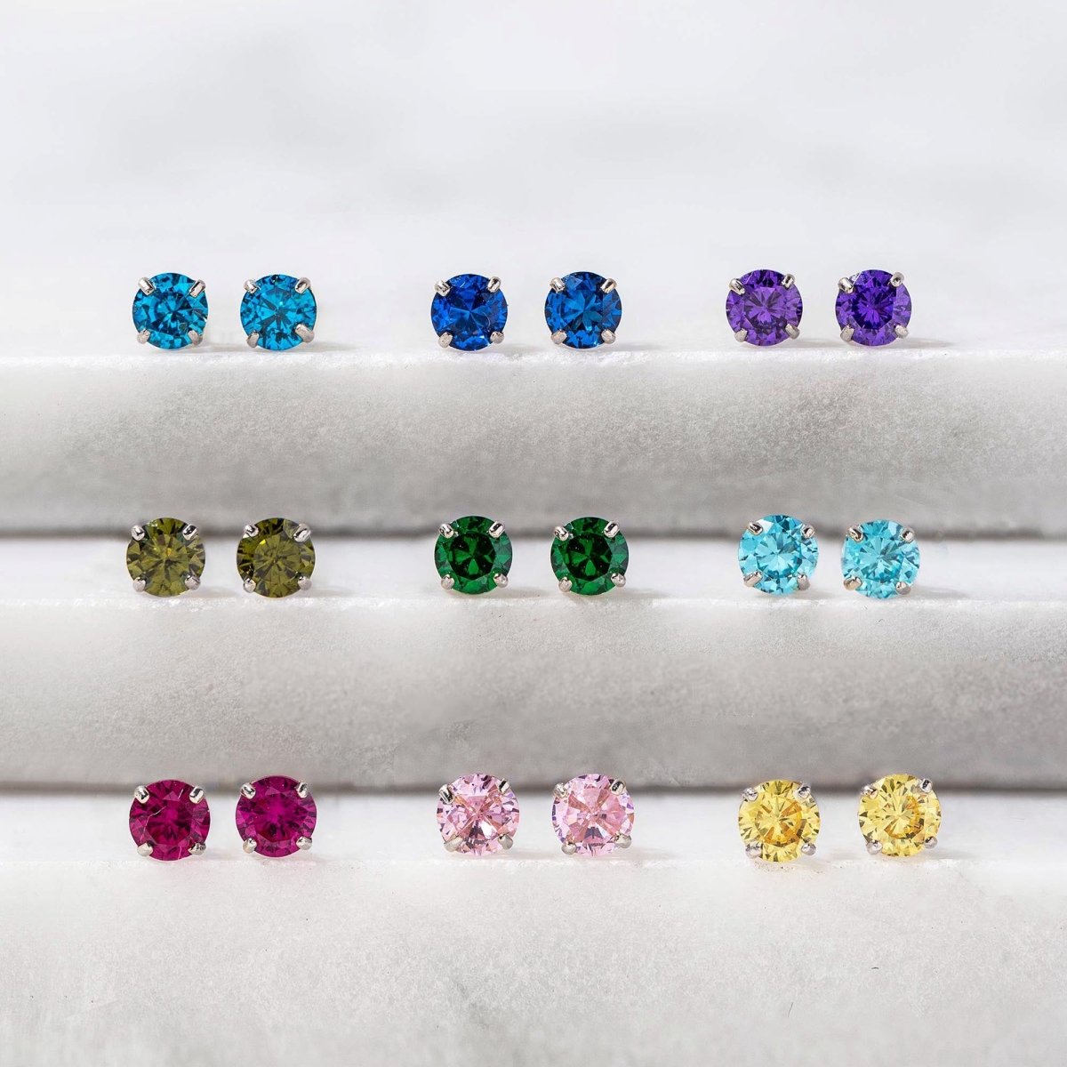14K white gold round birthstone studs in assorted colors arranged in rows on marble ledges