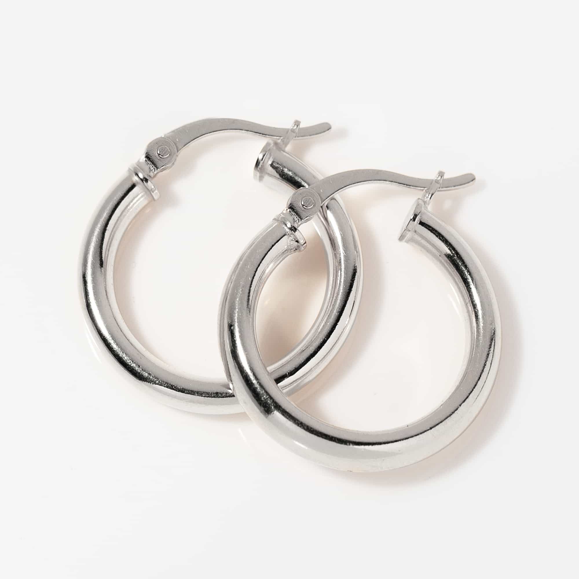 Sterling silver thick tube hoop earrings laid on a white background, close-up detail