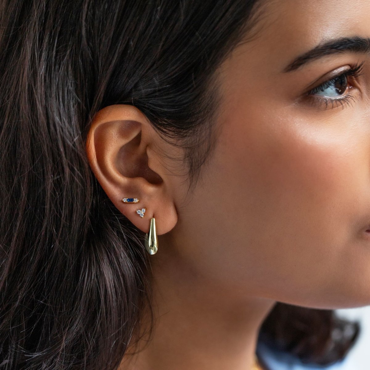 Close up of woman's ear featuring Gold Vermeil Gemstone Bar + Clover Studs Set Blue Sapphire and chunky hoop earring