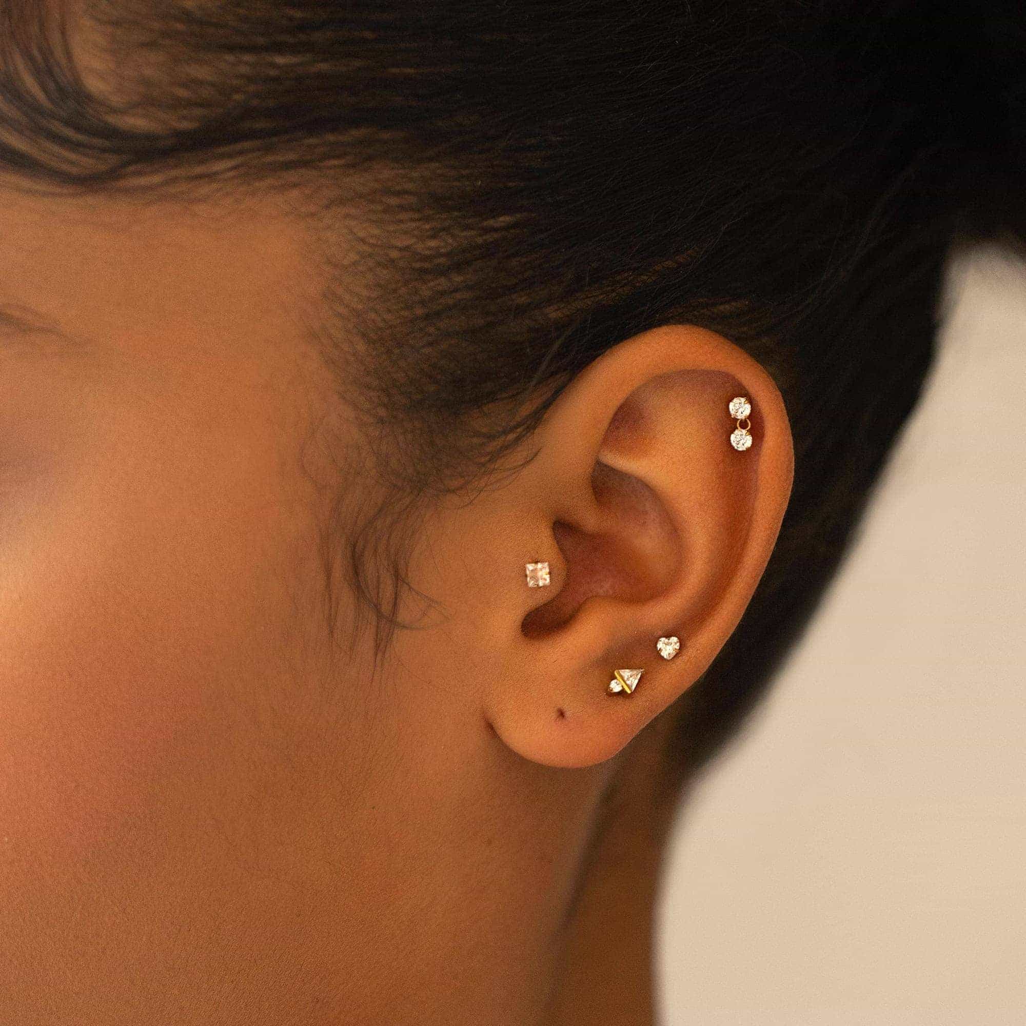 Gold clear-stone flat back studs in heart, triangle and square shapes shown on a model's ear