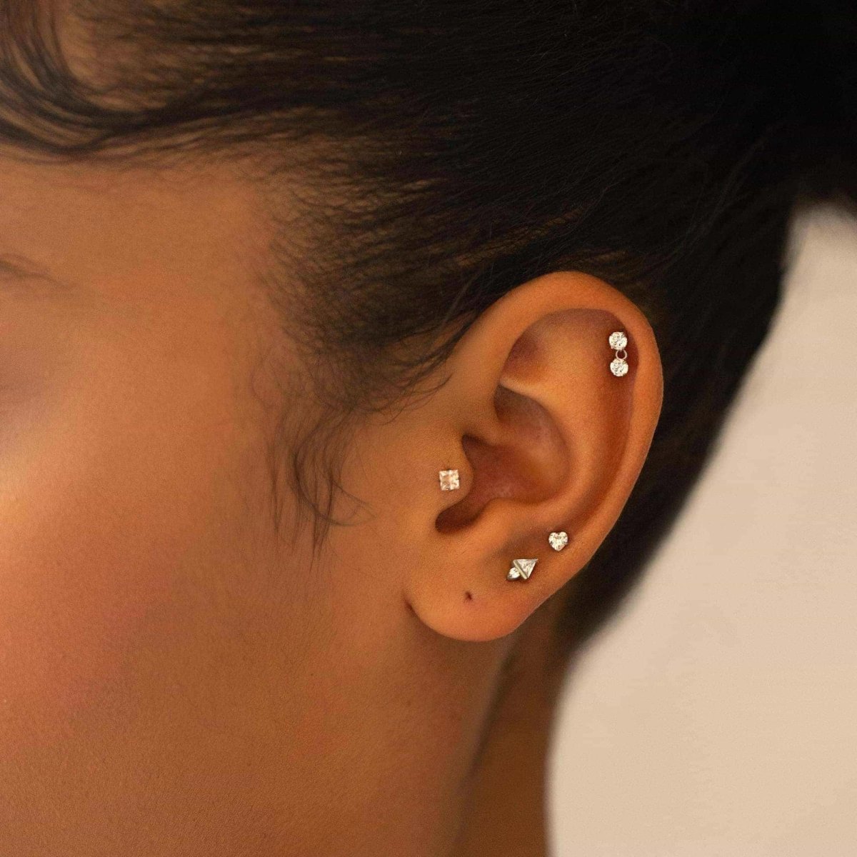 Gold clear-stone flat back studs in heart, square and triangle shapes shown across a model's ear