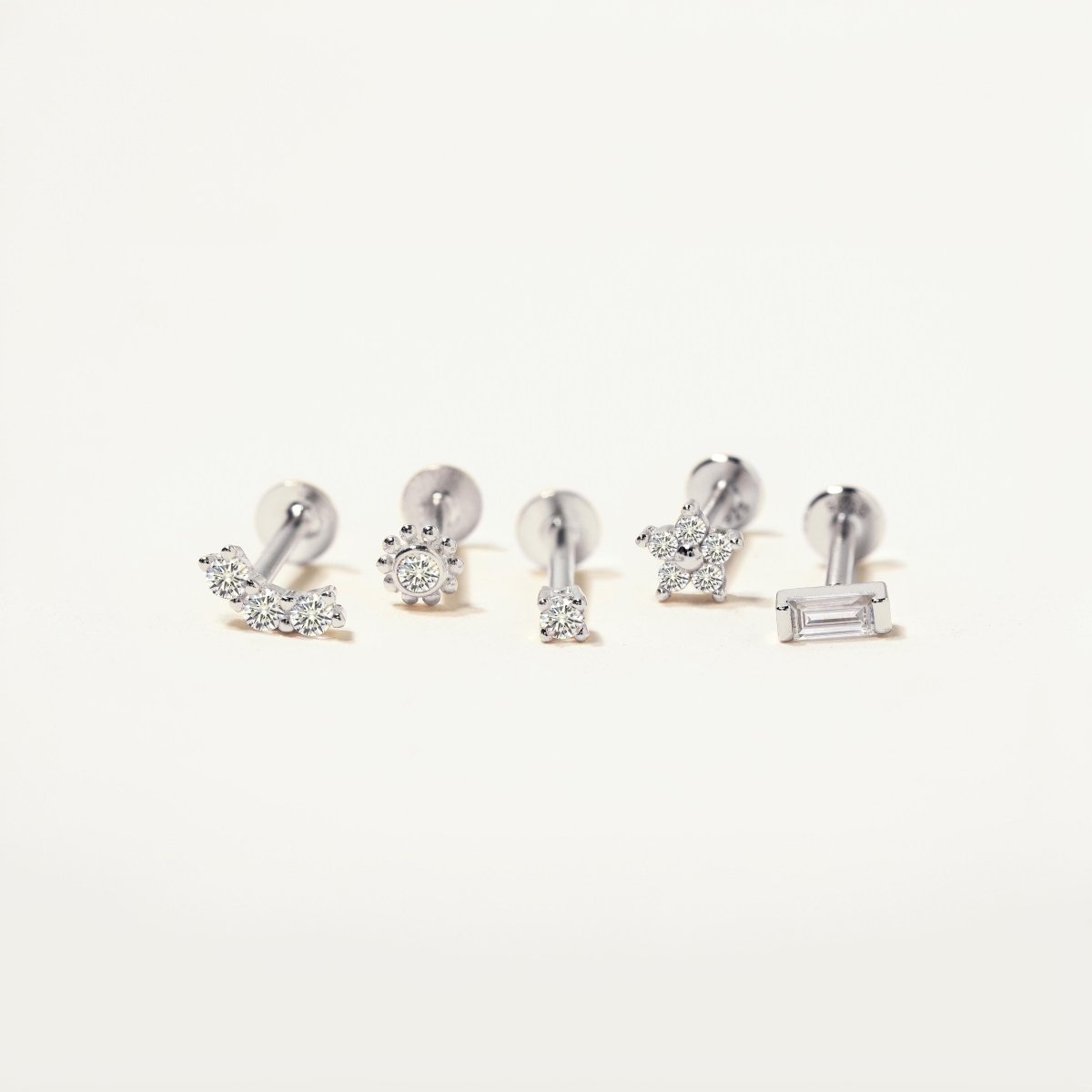 Five sterling silver flat back stud styles with clear stones, including a baguette bar, on a white background