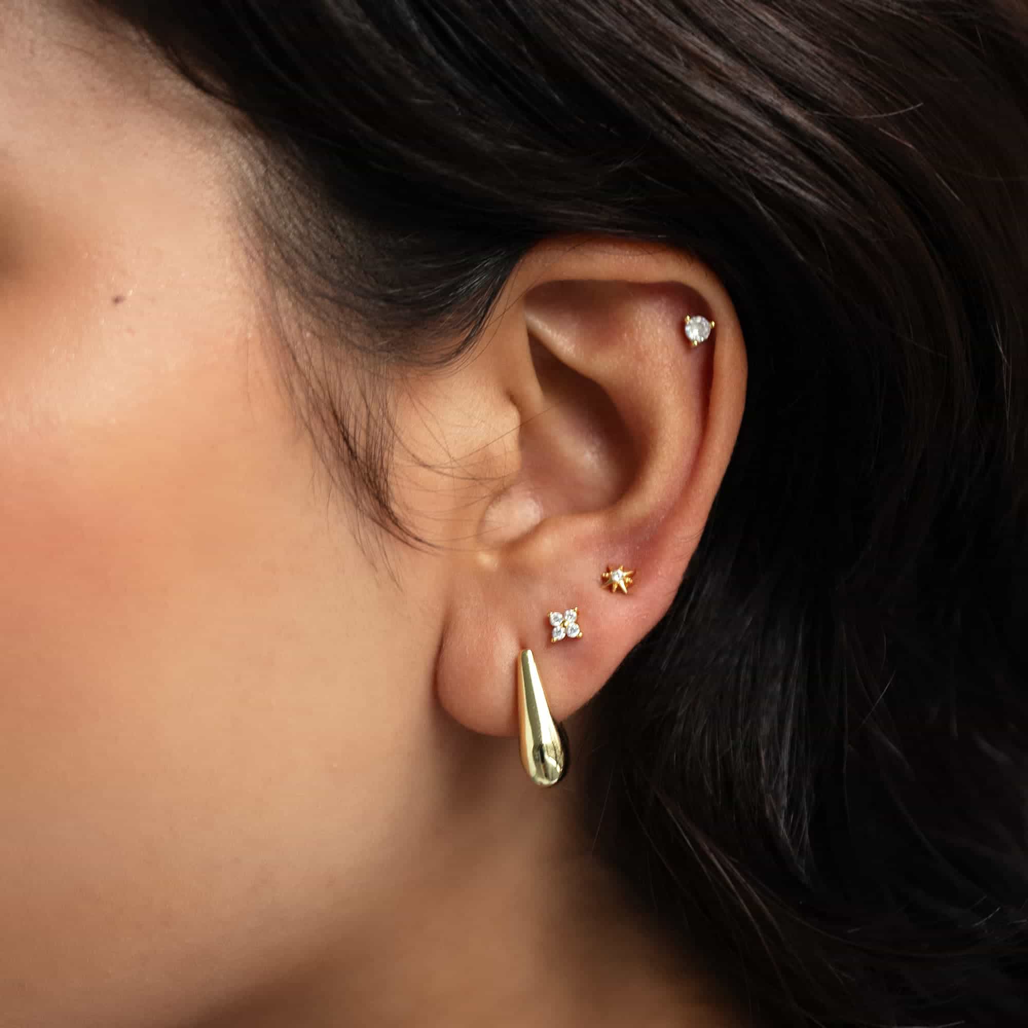 Gold teardrop hoop with star, clover, and clear-stone studs on a model's ear