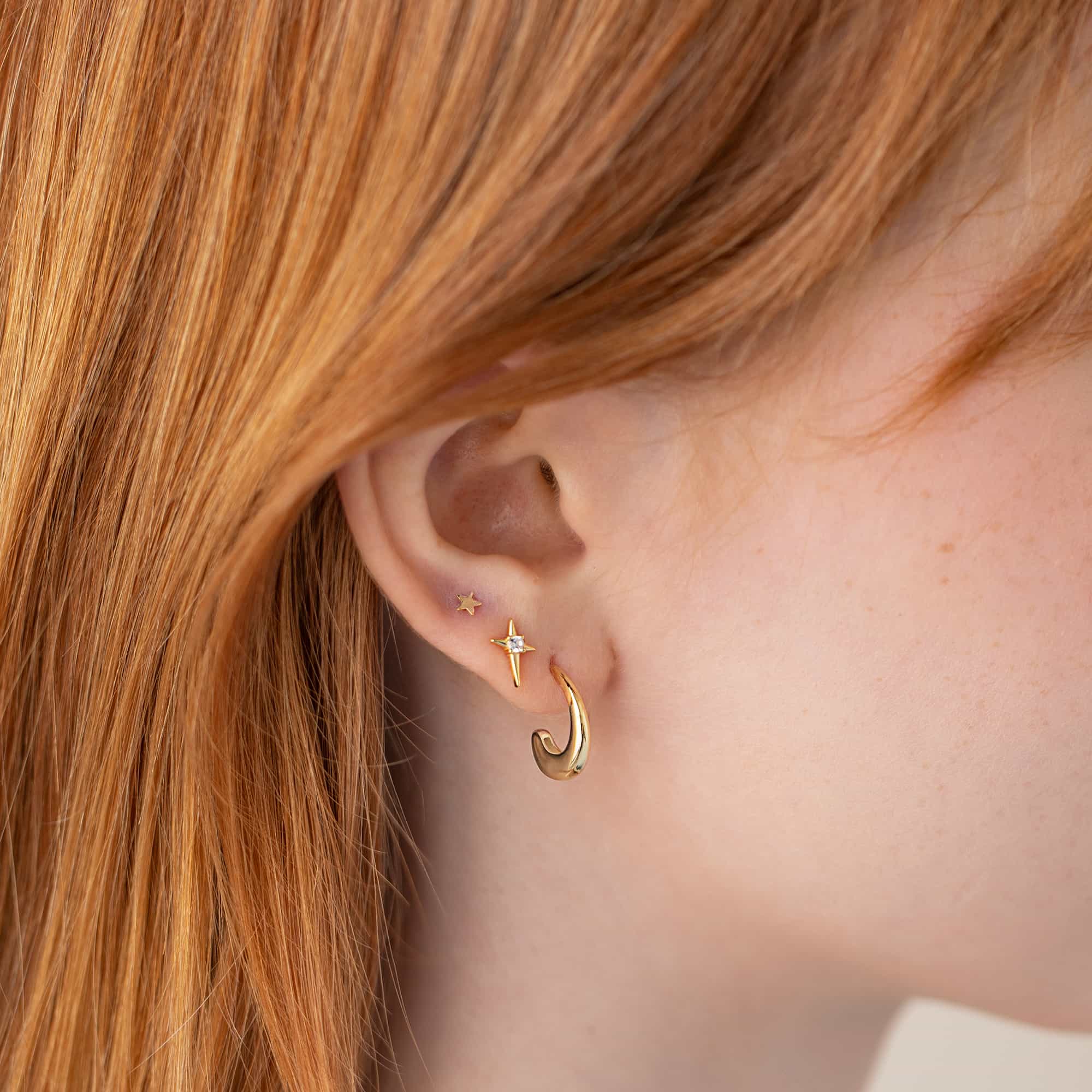 Gold small J-hoop and a tiny star stud with a clear stone, shown on a model's lobe