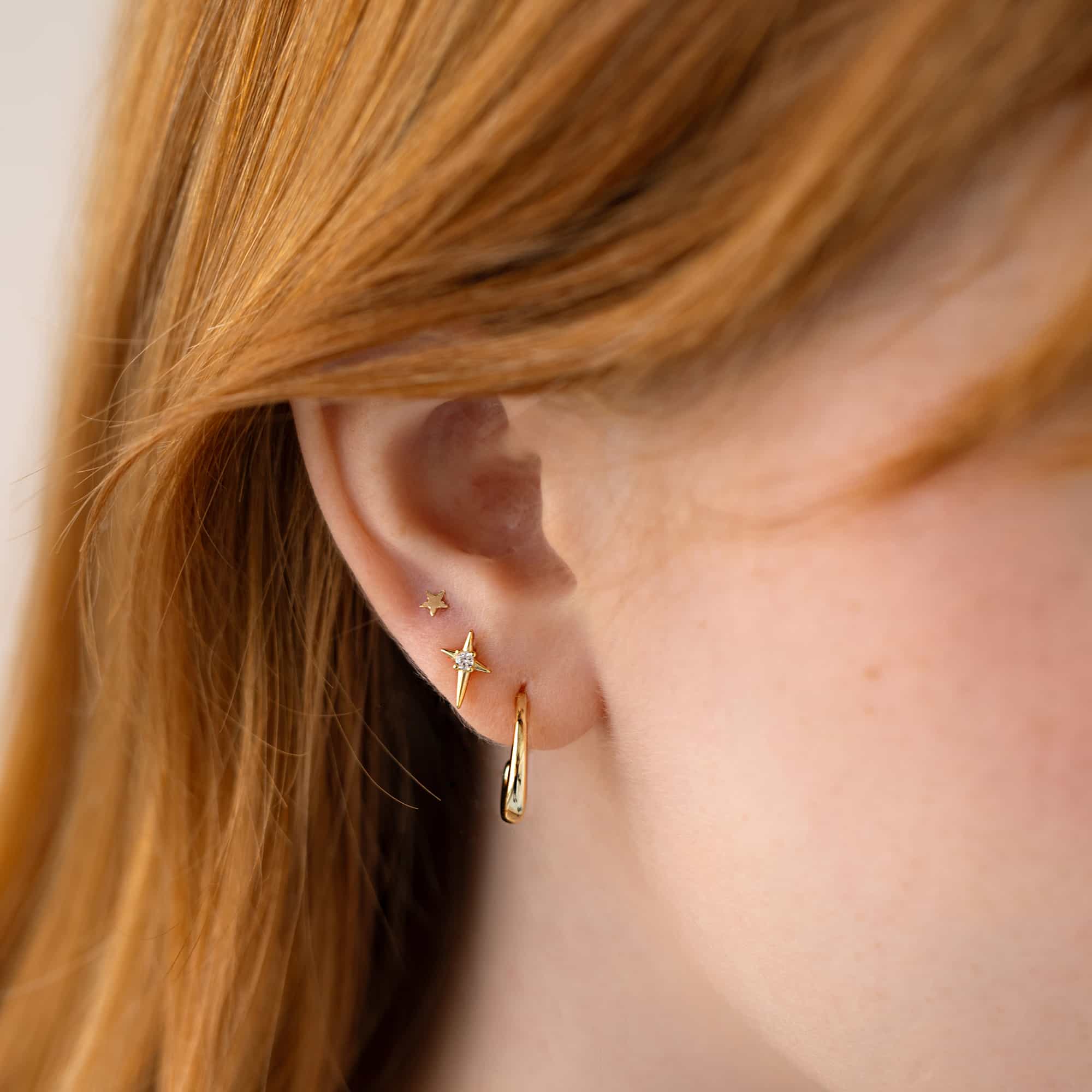 Gold star, starburst and hoop earrings shown in a lobe ear stack on a model