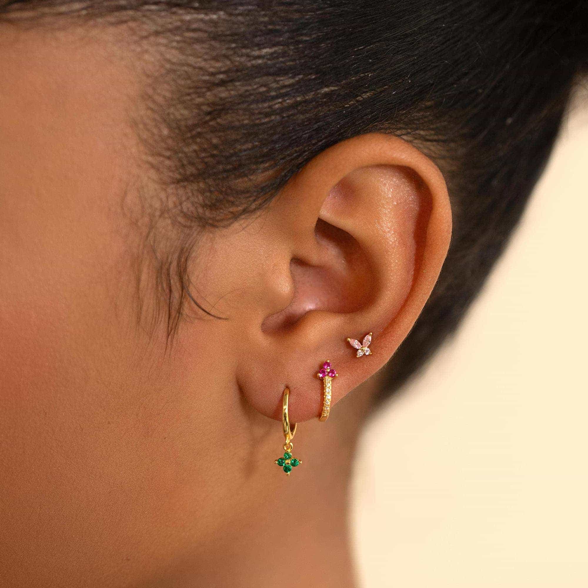 Gold huggie and stud earrings with green, pink and clear stones, stacked on a model's ear