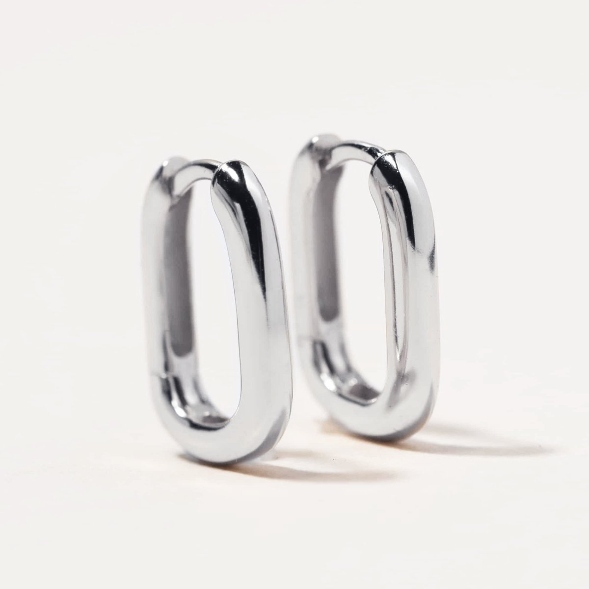 Pair of sterling silver U-shaped huggie hoops with a smooth profile, on a cream background