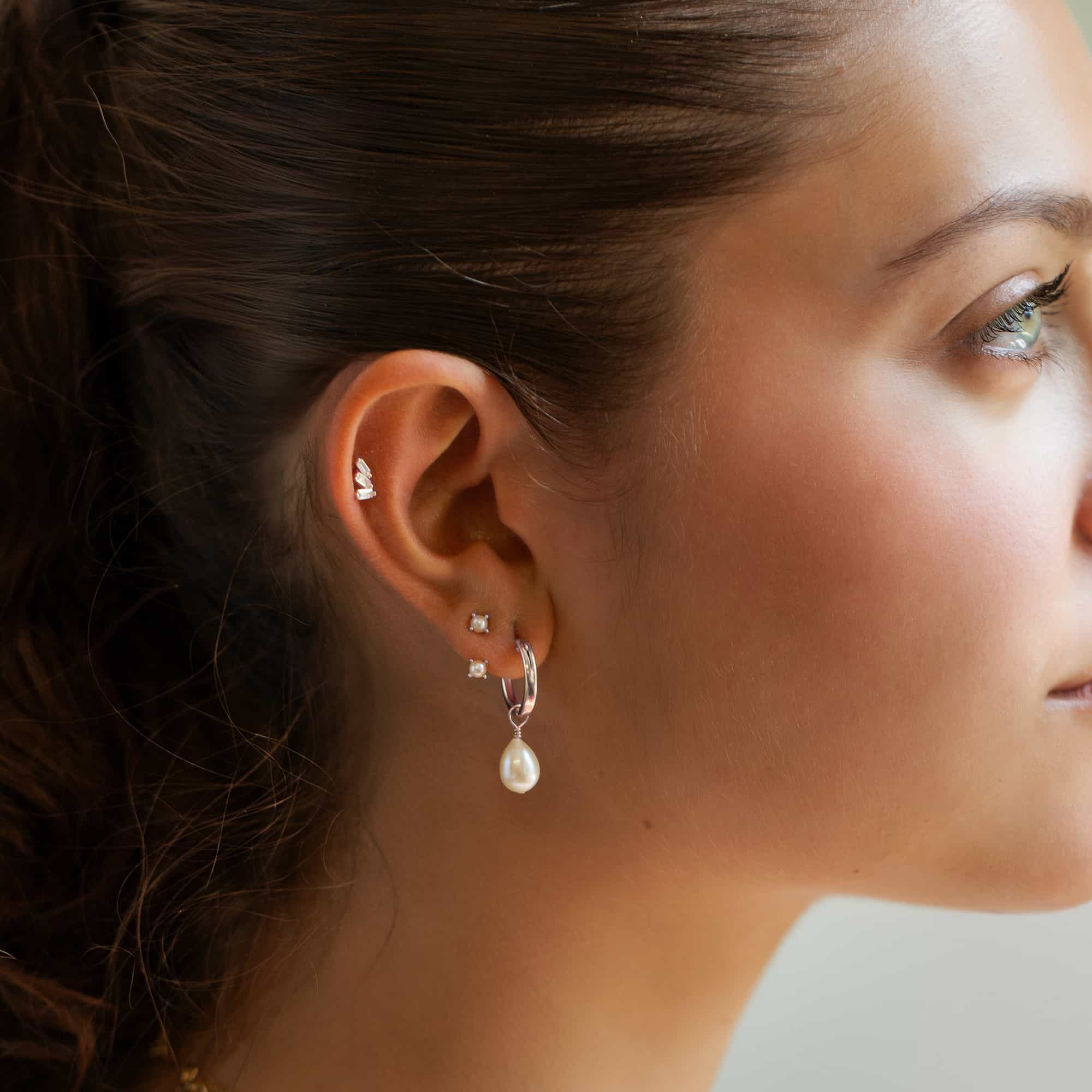 Silver ear stack with baguette studs, pearl studs and a teardrop pearl hoop, shown on a model's ear