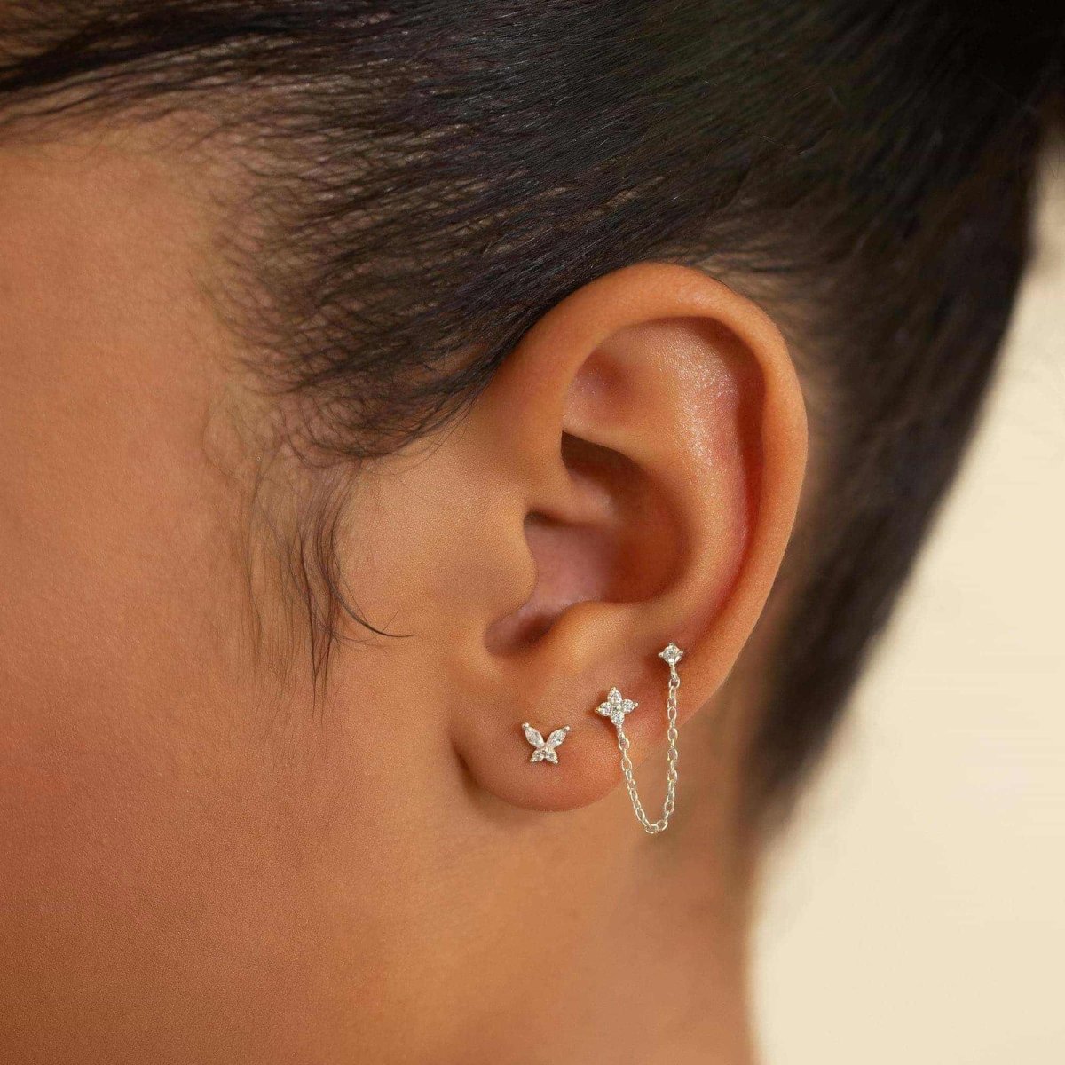 Sterling silver pavé chain studs with clear stones and a draped chain, shown on a model's ear